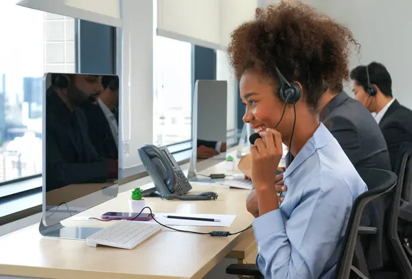 Çağrı merkezinde iletişim kurmak ve hizmet vermek için kulaklık kullanan genç bir Afrikalı Amerikalı kadın, iş kadını operatör modern ofis telefonlarına cevap veriyor