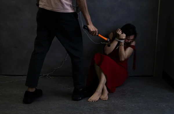 woman afraid in red being tied, psycho killer man holding hammer threatening to female victim,concept of women victim,hostage,crime,violence