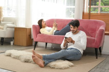 husband and wife spend their free time on weekend by using mobile phones in living room,young interracial couple relaxing at home together concept of family,relationship,holiday,resting