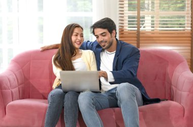 husband and wife spend free time on weekend together,using laptop in living room,young interracial couple relaxing at home,concept of family,relationship,holiday,resting