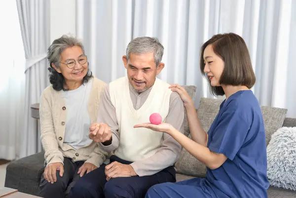 young female helper teaching older adult man for exercise hands with a ball,an asian nurse visit asian senior family at home,concept of elderly people health care,homecare,home health nursing