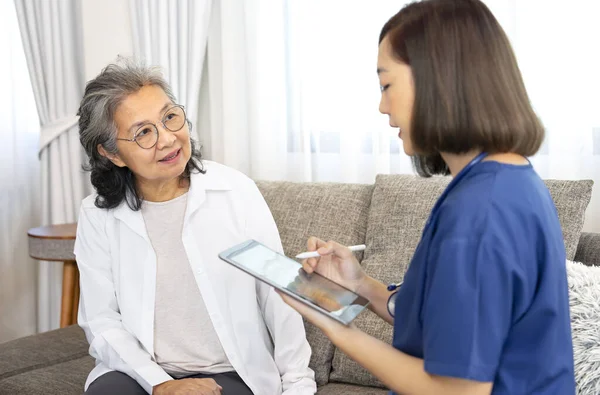 A senior woman giving a health interview to a home visiting nurse at home, a young female expertise healthcare talking and collecting data on tablet computer,concept of home care,home health care