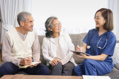 Yaşlı çiftin evde kalan bir hemşireyle konuşması, genç kadın hemşire, evde tablet kullanarak kendi sağlık hizmetini tavsiye etmesi, yaşlı adamın not alması, yaşlı ev bakımı, evde bakım konsepti, 