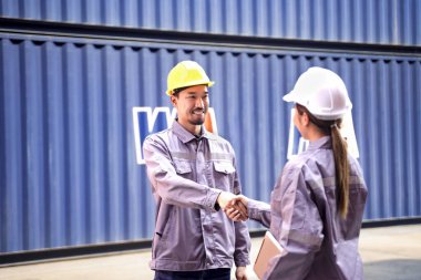 İki Asyalı iş arkadaşı, kargo konteynırının kooperatifi veya denetiminin başarıyla tamamlanması için nakliye sahasında işlerini bitirdikten sonra el sıkışıyor.