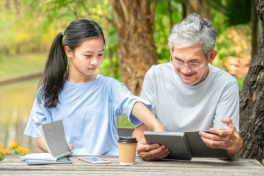 Asyalı genç kız büyükbabasıyla kitap okuyor, mutlu aile torunu ve büyükbabası bahçede birlikte vakit geçiriyorlar, aile hayatı, ilişki, ergen yetiştirme kavramları.