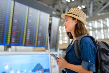 Sırt çantalı genç Asyalı kız elinde pasaport ve uçuş kartı ile kapıya zamanında varmak için uçuş saatine bakıyor ve kontrol ediyor.