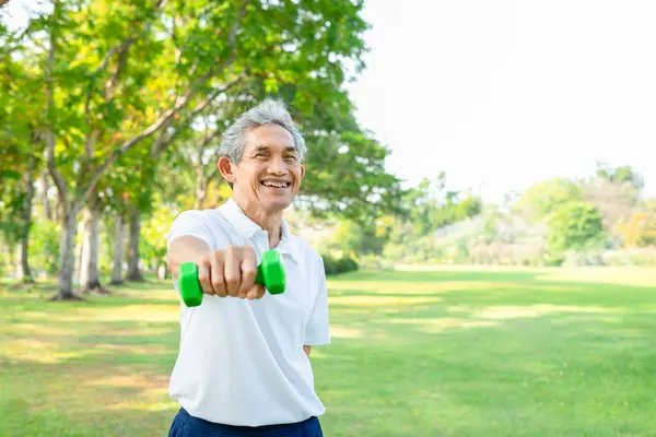 portrait asian senior man lifting dumbbell laughing and looking at camera,older adult male exercise in the summer park,elderly health care,wellness,wellbeing