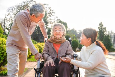 80 yıldır tekerlekli sandalyede oturan Asyalı kadın portresi. Ailesi onunla parkta ilgileniyor. Aile hayatı, yaşlı sağlık hizmetleri, ilişki...