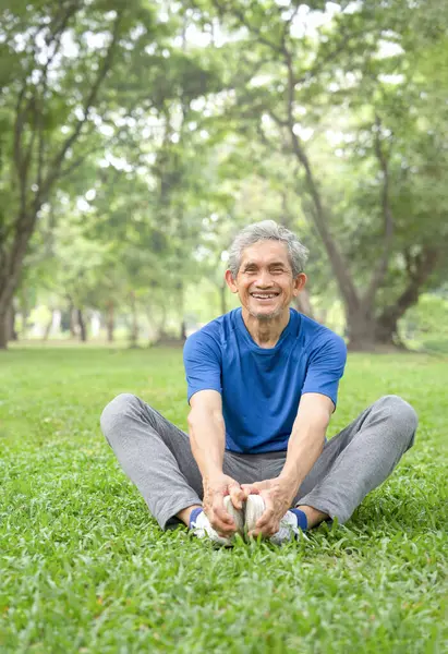 asian senior man with grey hair sitting on grasses in the park,stretching his legs before exercise in the morning,concept prevent of injury, promote blood flow in elder people