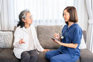 Evde üniformalı bir hemşire, mevcut hastalık geçmişi hakkındaki konuşmaları dinliyor, tablet bilgisayar kullanarak veri topluyor, evde bakım, evde sağlık hizmetleri kavramını kullanıyor.