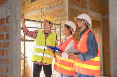 Genç Asyalı elektrikçi inşaat alanında çalışan müteahhit ekibe elektrik tesisatı hattını anlatıyor. 