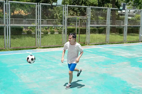 stock image image of young asian man running to follow and keep his eye on the ball in the air while practicing in the stadium, concept for people workout,football or futsal game 