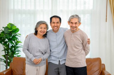 Orta yaşlı Asyalı bir erkek ile orta yaşlı Asyalı bir çiftin portresi. Oturma odasında duruyor. Aile hayatı, ilişki, ev hayatı.