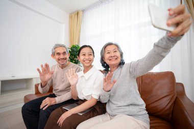 Asyalı genç torun, iki kuşak boyunca dedelerini ziyaret ediyor. Modern yaşam tarzına sahip büyükannesi akıllı telefon kullanıyor. Oturma odasında selfie çekiyor.