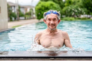 Yüzme havuzunda gözlüklü mutlu yaşlı bir adam. Sağlıklı Asyalı son sınıf öğrencisi. Tatilin tadını çıkarıyor.