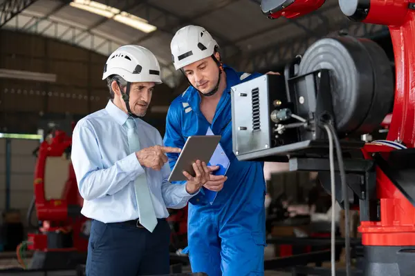 Üst düzey uzman yönetici tablet bilgisayar kullanarak genç bir beyaz teknisyene bakım robotu makinesi sorununu öneriyor.