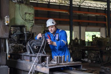 Güvenlik dişlisi genç beyaz teknisyen kaynak fabrikasında endüstriyel makineleri inceliyor ve onarıyor.