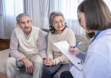 Asyalı üst düzey bir çift, ev ziyaretçisi bir hemşireye sağlık görüşmesi yapıyor. Genç bir kadın sağlık personeli, hasta veri notlarını parmak şıklatma çizelgesi kağıdına, yaşlı sağlığı kavramına, evde bakım hizmetlerine götürüyor.