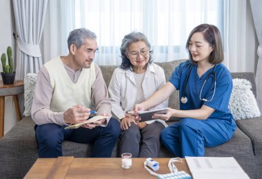 Yaşlı çiftin evde kalan bir hemşireyle konuşması, genç kadın hemşire, evde tablet kullanarak kendi sağlık hizmetini tavsiye etmesi, yaşlı adamın not alması, yaşlı ev bakımı, evde bakım konsepti, 
