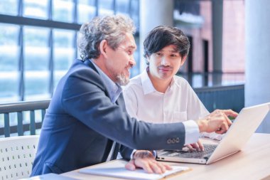 Genç Asyalı bir adam oturuyor ve danışman öğretmen ile konuşuyor, profesör diz üstü bilgisayarlı üniversite öğrencisine tavsiye veriyor.