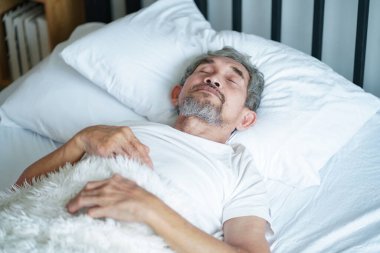 Yatakta uyuyan yaşlı bir adam, battaniyede rahat uyuyan yaşlı bir erkek. konsept yaşlılar yaşam tarzı, yeterince dinlenme, sağlık hizmetleri                                                                     