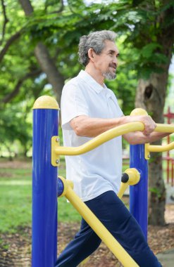 Neşeli son sınıf öğrencisi ovate stepper jimnastik aletleri üzerinde egzersiz yapıyor. Doğa parkında olgun erkek egzersizleri yapıyor. Yaşlılar için sağlık hizmetleri, sağlık hizmetleri, refah...                