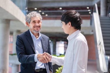 Profesör, üniversite öğrencisine tavsiye verdikten sonra tokalaşıyor. Genç Asyalı adam binada duruyor ve danışman öğretmenle konuşuyor.