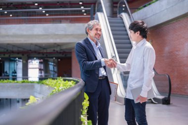 Profesör, üniversite öğrencisine tavsiye verdikten sonra tokalaşıyor. Genç Asyalı adam binada duruyor ve danışman öğretmenle konuşuyor.