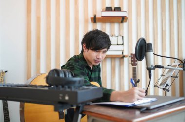 Asyalı müzisyen müzik stüdyosunda kulaklık takar, gitar çalar ve şarkı sözleri yazar.