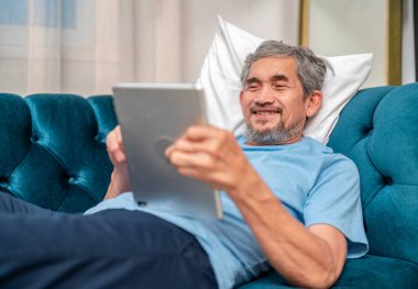 Son sınıf öğrencisi kanepede dinleniyor. Tablet kullanıyor. Evdeki aileyle, yaşlılarla ve teknolojiyle iletişim kuruyor.