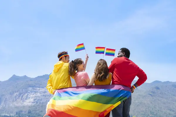 Bir grup farklı lgbtq arkadaş renkli kıyafetler giyiyorlar, yan yana duruyorlar, gülümsüyorlar ve havada lgbt bayrakları sallıyorlar, lgbt topluluğunun eşitlik hareketini destekliyorlar ve haziranda lgbt 'ın mutlu gurur ayını kutluyorlar