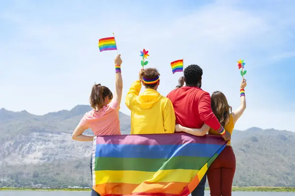 Bir grup farklı lgbtq arkadaş renkli kıyafetler giyiyorlar, yan yana duruyorlar, gülümsüyorlar ve havada lgbt bayrakları sallıyorlar, lgbt topluluğunun eşitlik hareketini destekliyorlar ve haziranda lgbt 'ın mutlu gurur ayını kutluyorlar
