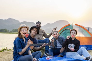 Çeşitli arkadaş grupları göletin kenarında kamp yaparken eğleniyorlar. Asyalı aile ve Afrikalı arkadaş akşam güneşinde müzik çalıp yemek yiyorlar.