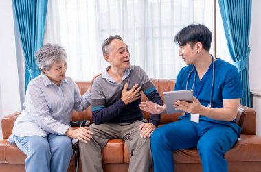 Asyalı üst düzey çift, ev ziyaretçisi hemşireye sağlık mülakatı yapıyor. Genç erkek hemşire, uygulamalar, yaşlı sağlık hizmetleri, ev sağlığı hizmetleri, ev sağlığı hizmetleri gibi konularda tavsiye vermek için tablet kullanıyor.