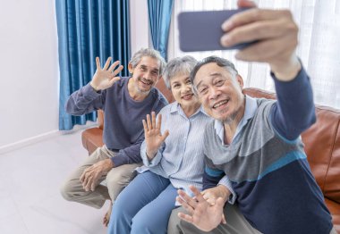 Mutlu Asyalı üst düzey aile ve arkadaşları evdeki kanepede otururken selfie çekiyorlar. Yaşlılar yaşam tarzı, aile ilişkisi, arkadaşlık, toplantı.