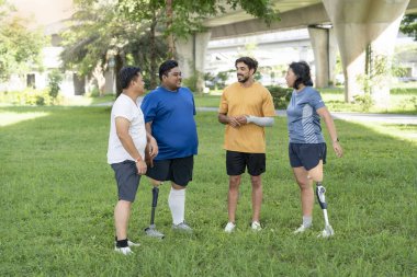 Parkta toplanan çok ırklı arkadaş grubu, protez bacaklı atletik insanlar dışarıda egzersiz yaparken arkadaşlarıyla konuşmaktan zevk alıyorlar.