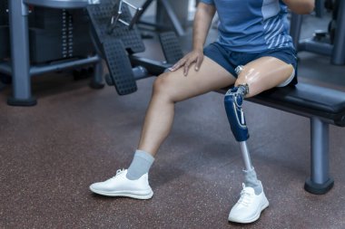 Beden eğitiminde protez bacağı olan, spor aletlerinin üzerinde oturan spor salonunda çalışan bir kadın.