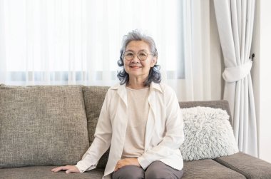 Oturma odasındaki kanepede oturan Asyalı son sınıf öğrencisi bir kadının portresi. Yaşlılık hayatı, ev hayatı.