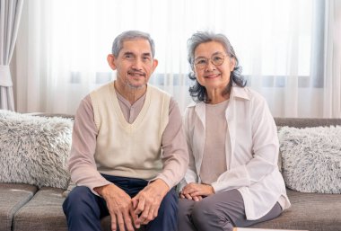 Oturma odasındaki kanepede oturan Asyalı yaşlı çift portresi. Yaşlılar, ev hayatı.