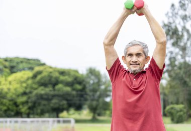 Doğa parkında halterle egzersiz yapan aktif kıdemli bir adam. Yaşlılar için yaşam tarzı, spor aktiviteleri, doğa için sağlık sigortası.