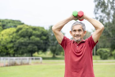 Doğa parkında halterle egzersiz yapan aktif kıdemli bir adam. Yaşlılar için yaşam tarzı, spor aktiviteleri, doğa için sağlık sigortası.