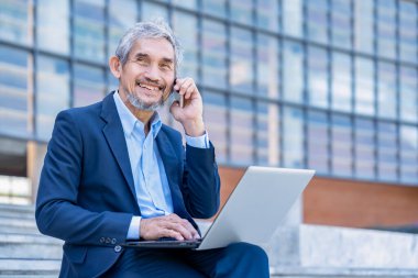 Dizüstü bilgisayarı olan, gülümseyen, dışarıda cep telefonuyla konuşan deneyimli bir iş adamı. 