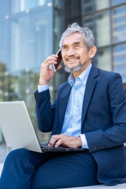 Dizüstü bilgisayarı olan, gülümseyen, dışarıda cep telefonuyla konuşan deneyimli bir iş adamı. 