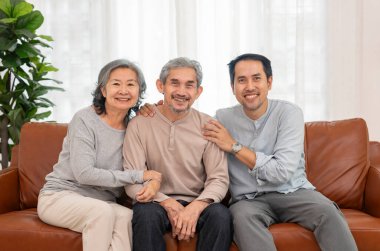 Orta yaşlı bir adamla birlikte mutlu Asyalı çift oturma odasında kameraya poz veriyor, tatil, aile ilişkisi, ev, hayat, aile hayatı.