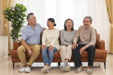 Mutlu Asyalı son sınıf çifti kanepede oturuyor, birlikte konuşuyorlar, yaşlı emekliler evdeki oturma odasında toplanıyorlar.