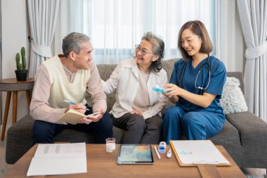 Asyalı kıdemli bir adam eşi için not alırken, konuk bir hemşire de ilaç alma, yaşlı sağlık hizmetleri, sağlık sigortası, evde sağlık hizmetleri gibi konularda tavsiye veriyor.