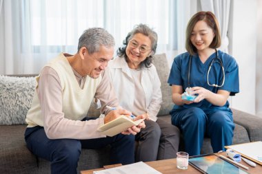 Asyalı kıdemli bir adam eşi için not alırken, konuk bir hemşire de ilaç alma, yaşlı sağlık hizmetleri, sağlık sigortası, evde sağlık hizmetleri gibi konularda tavsiye veriyor.