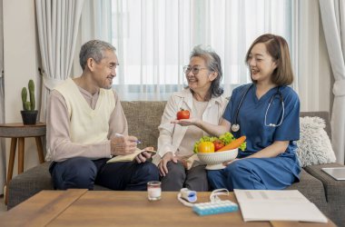 Ziyaretçi hemşire elinde bir kase sebze tutarken, Asyalı üst düzey çifte kendi sağlık hizmetleri, yaşlı sağlık hizmetleri, beslenme, sağlıklı yiyecekler, vitamin, organik gıdalar için tavsiye verirken, yaşlı adam not tutuyor