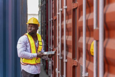 Güvenlik teçhizatlı Afrikalı bir adam konteynır kargosunda tablet bilgisayar kullanıyor, ustabaşı konteyner kutusundaki elektronik mührü kontrol ediyor, nakliye alanında çalışan bir işçi.