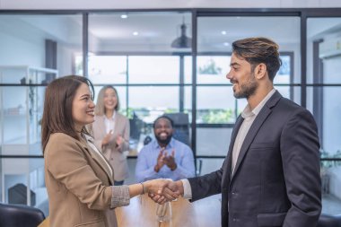 Ofis odasında çok ırklı iş ortaklığı toplantısı, Asyalı bir iş kadını gelecekteki iş birliği için beyaz iş adamıyla tokalaşıyor.